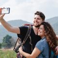 happy couple of travelers taking selfie on smartphone in nature in daytime